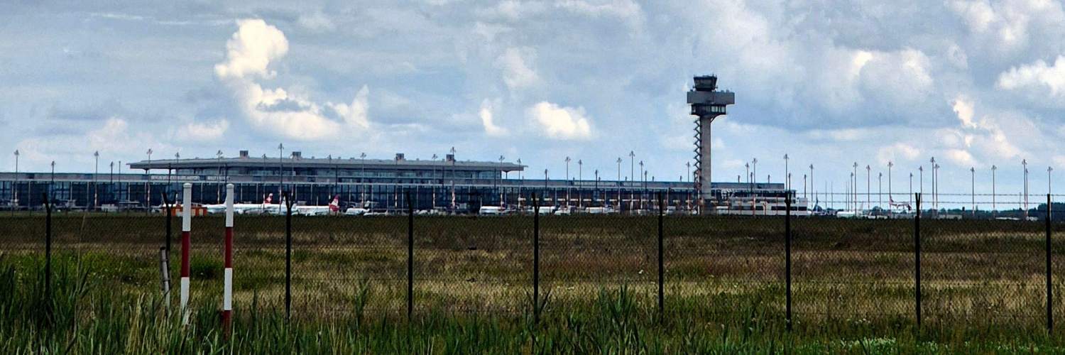 A view of Berlin Airport featuring a large terminal building in the background against a clear sky.
