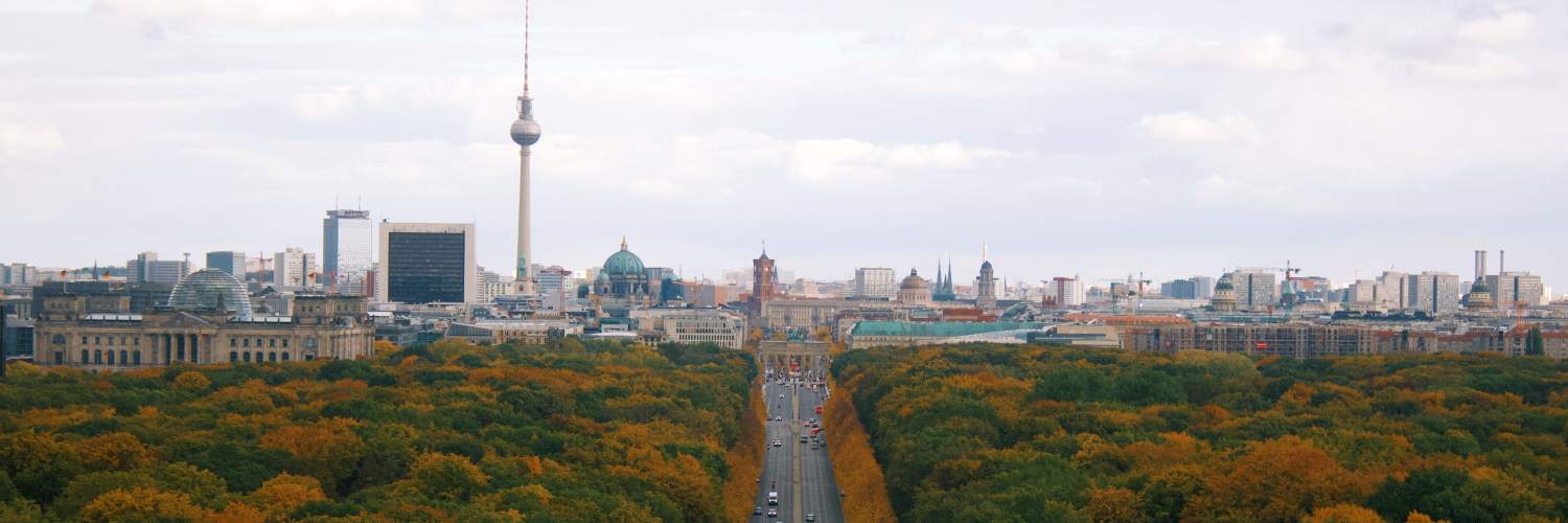 Berlin skyline in autumn, showcasing colorful foliage and iconic buildings against a clear blue sky.