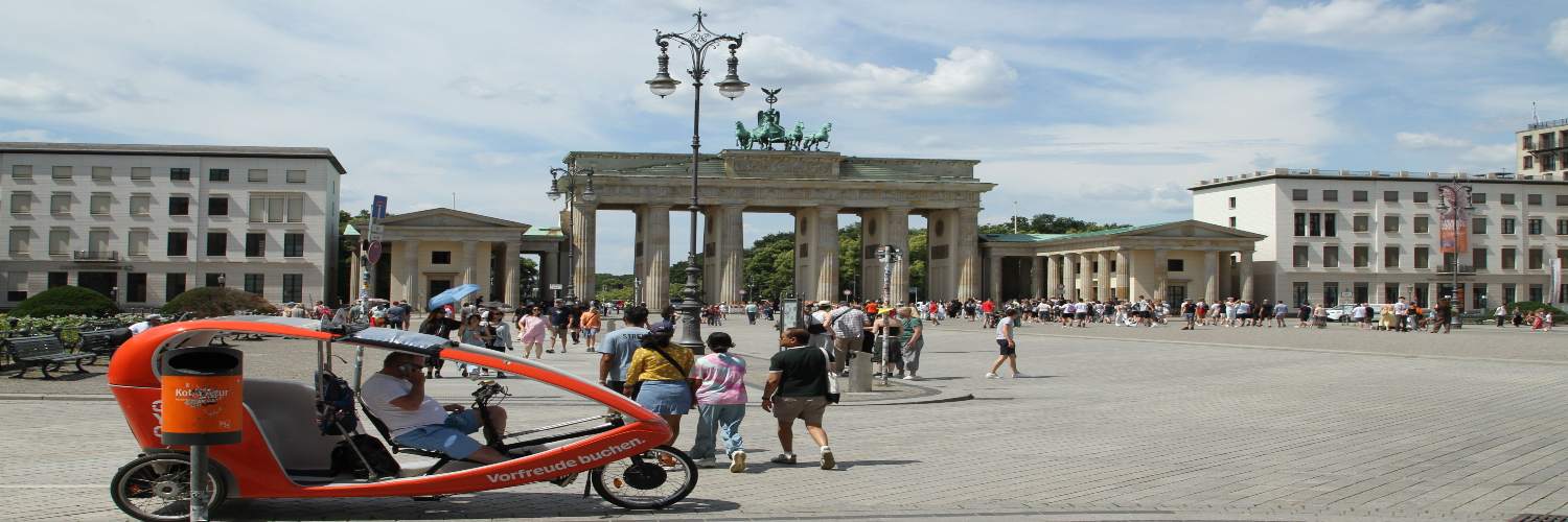 A bicycle taxi in Berlin under a clear blue sky with fluffy white clouds in the background.