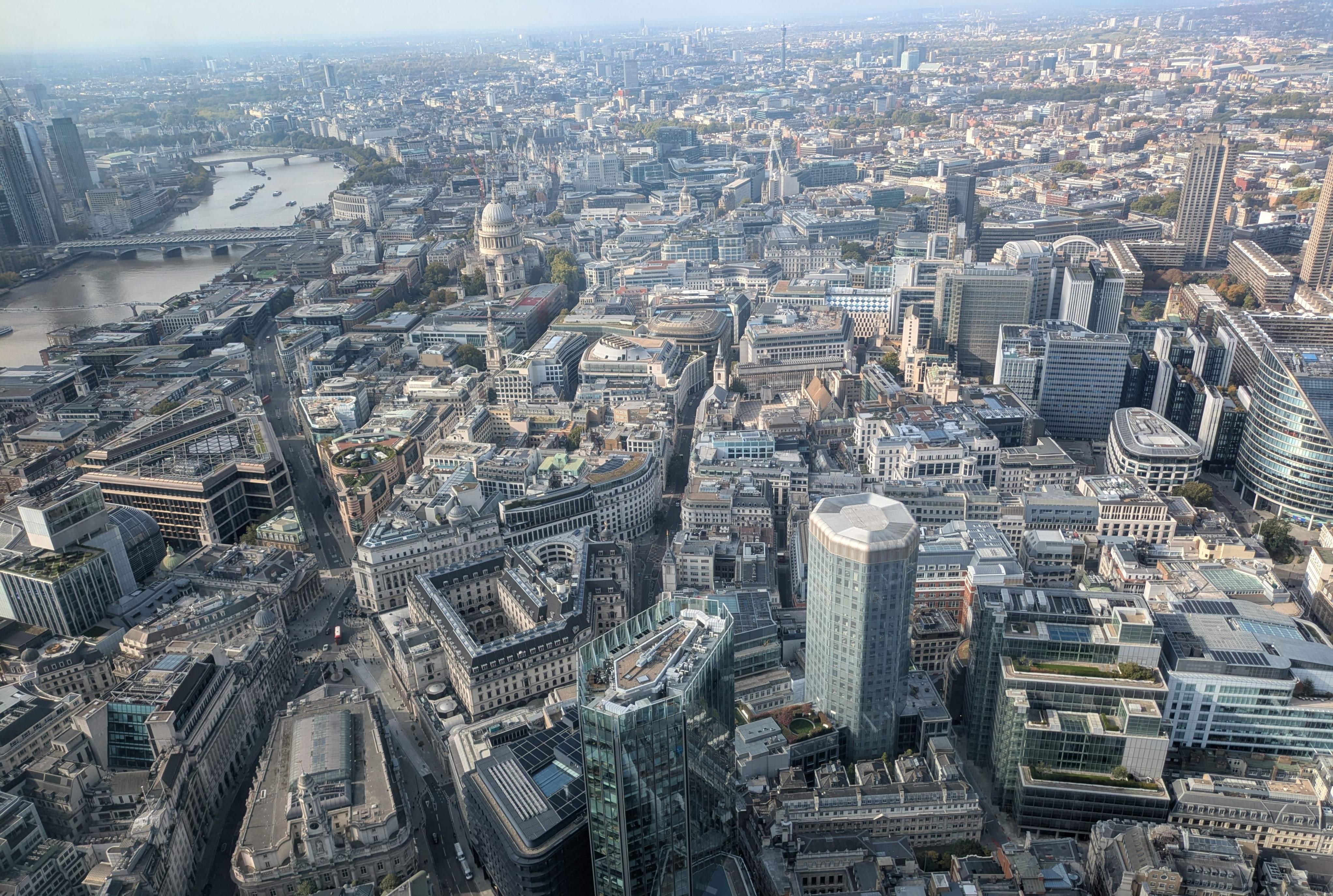 Aerial view of Central London showcasing iconic buildings, including the Gherkin, with a clear blue sky above.