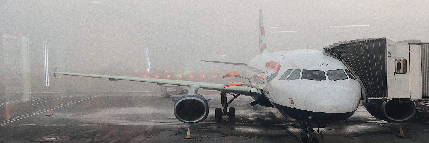 A plane parked on the tarmac at Gatwick Airport, surrounded by dense fog, obscuring visibility.