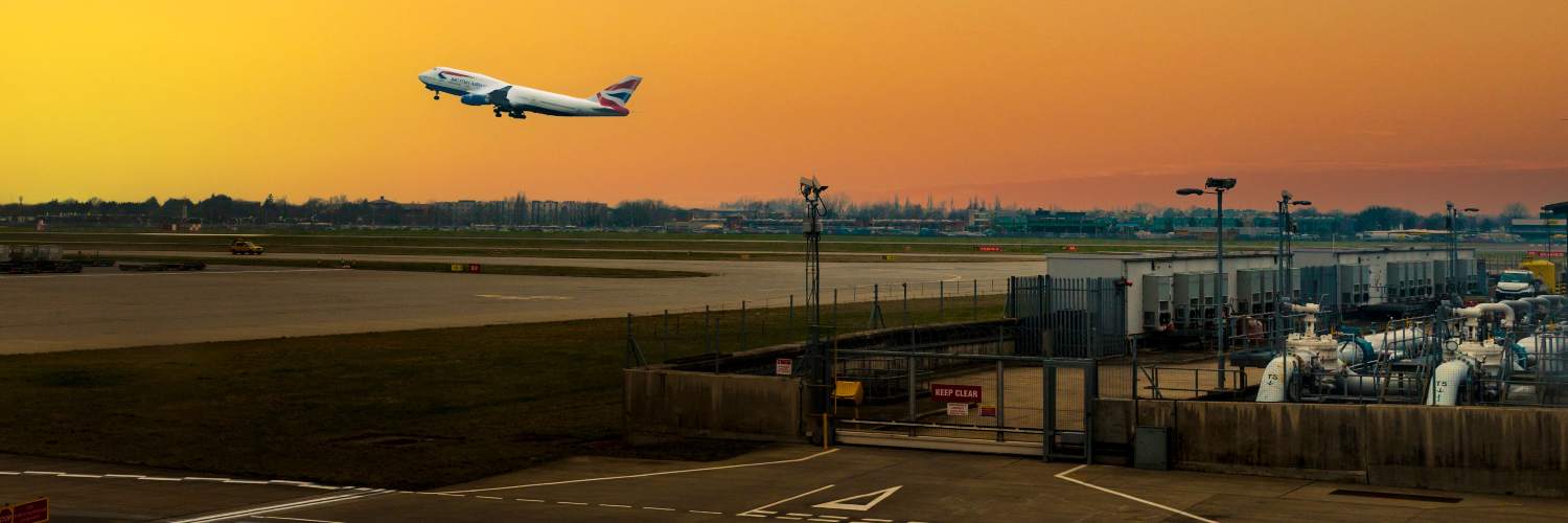 Airplane taking off from Heathrow Airport against a vibrant sunset sky.