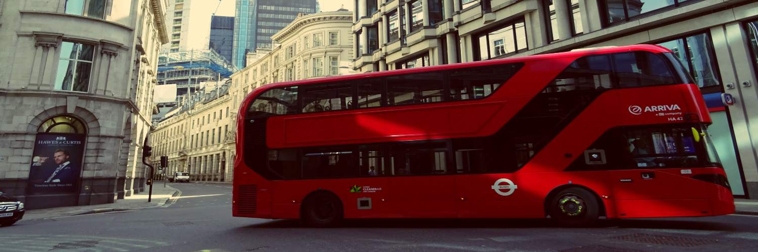 A red double-decker bus travels along a busy city street in London, showcasing urban life and transportation.