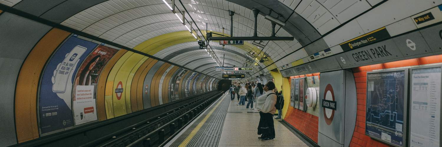A person waiting at a London subway station, surrounded by signage and train schedules.