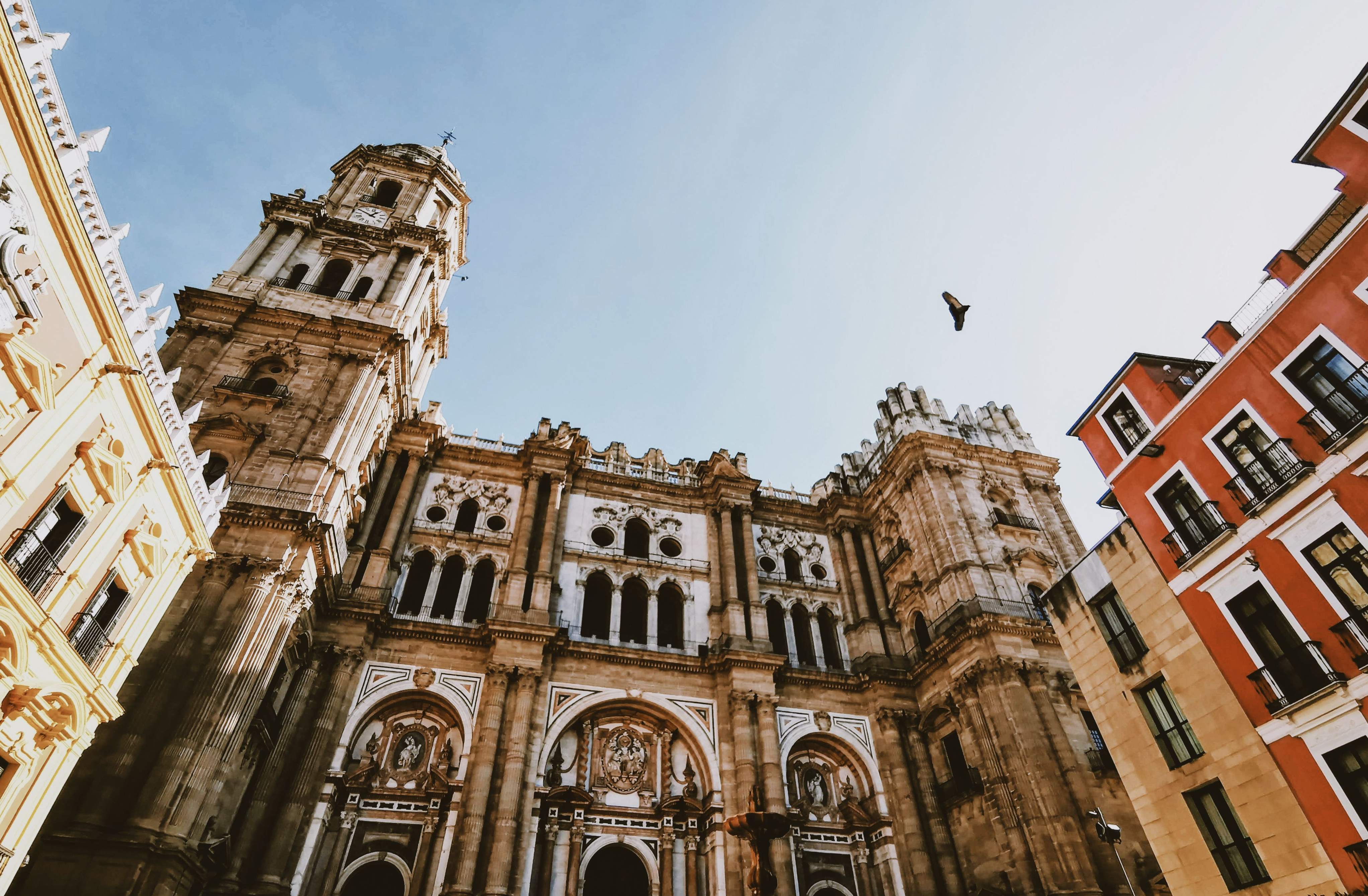 Malaga Cathedral’s ornate facade with historic architecture and towering bell structure under a clear sky.
