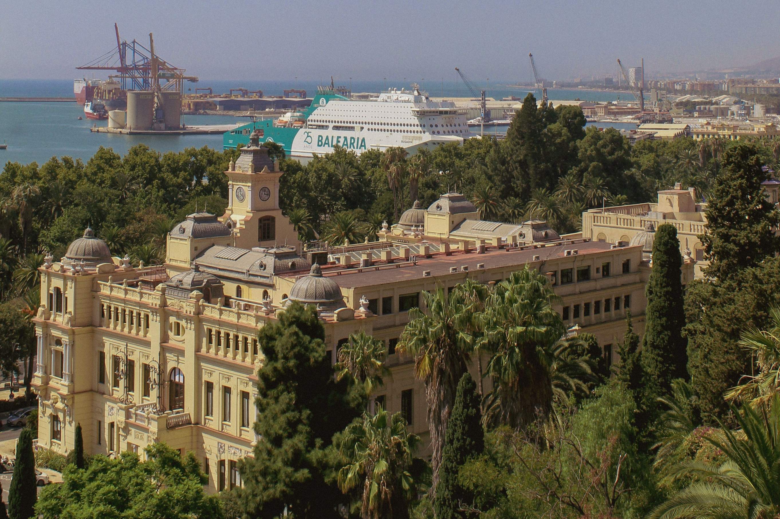 Panoramic view of Malaga's historic architecture with elegant buildings, lush gardens, and the Mediterranean port.
