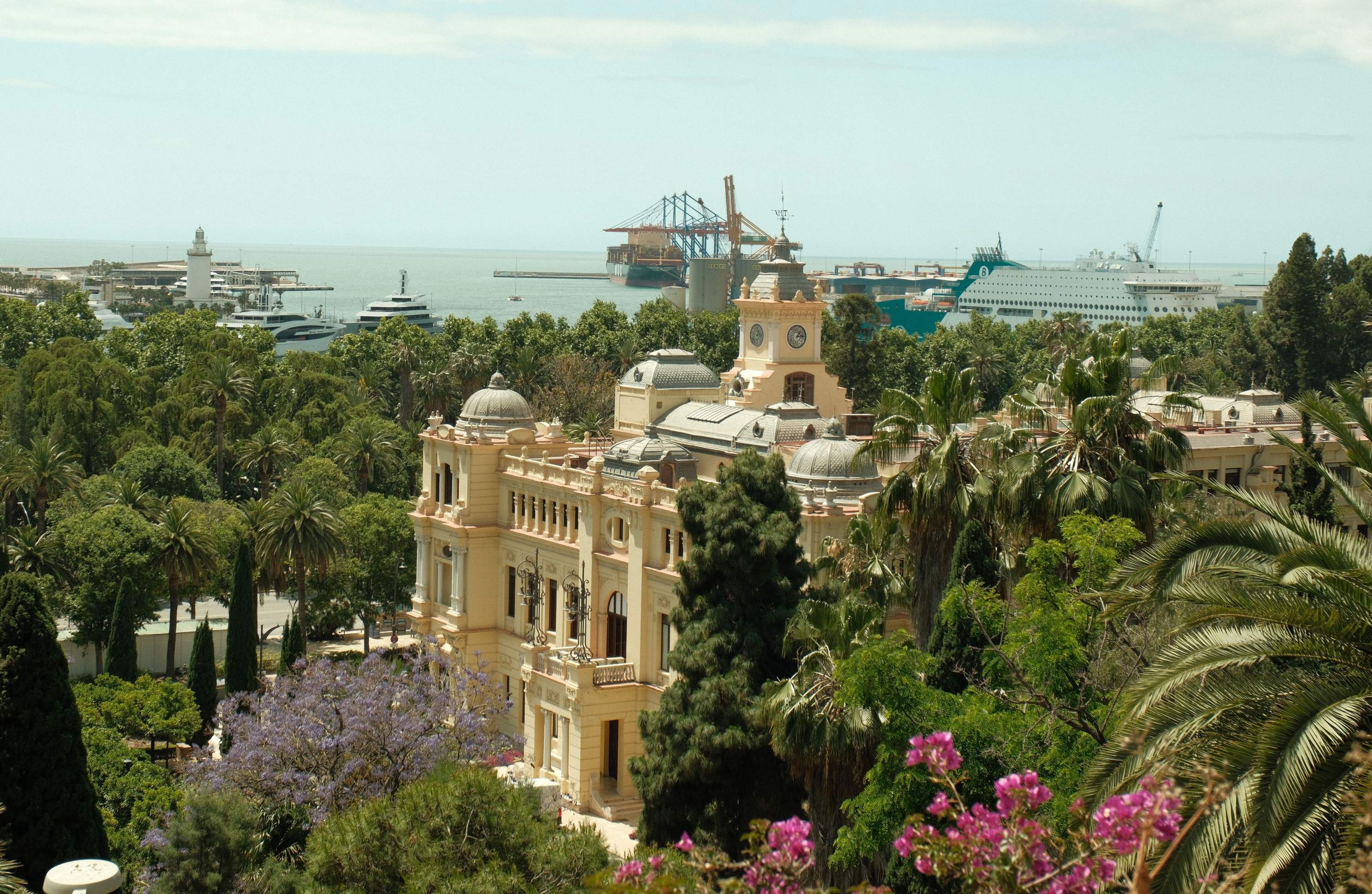 Historic building surrounded by lush gardens with Málaga's vibrant port, cruise ships, and Mediterranean coastline in the background.