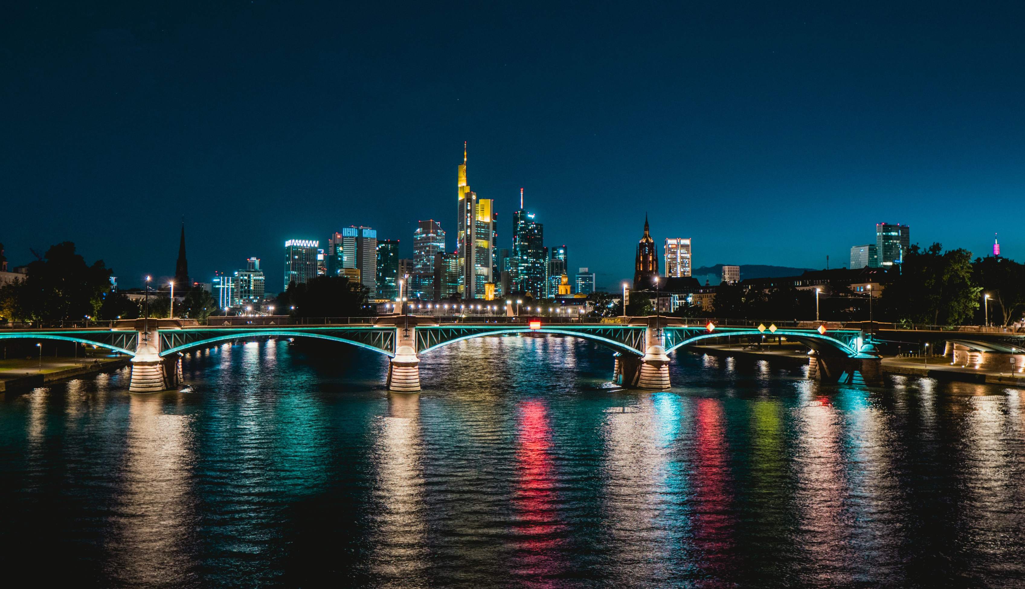 Night view of Frankfurt's skyline featuring an illuminated bridge and city lights reflecting on the water.