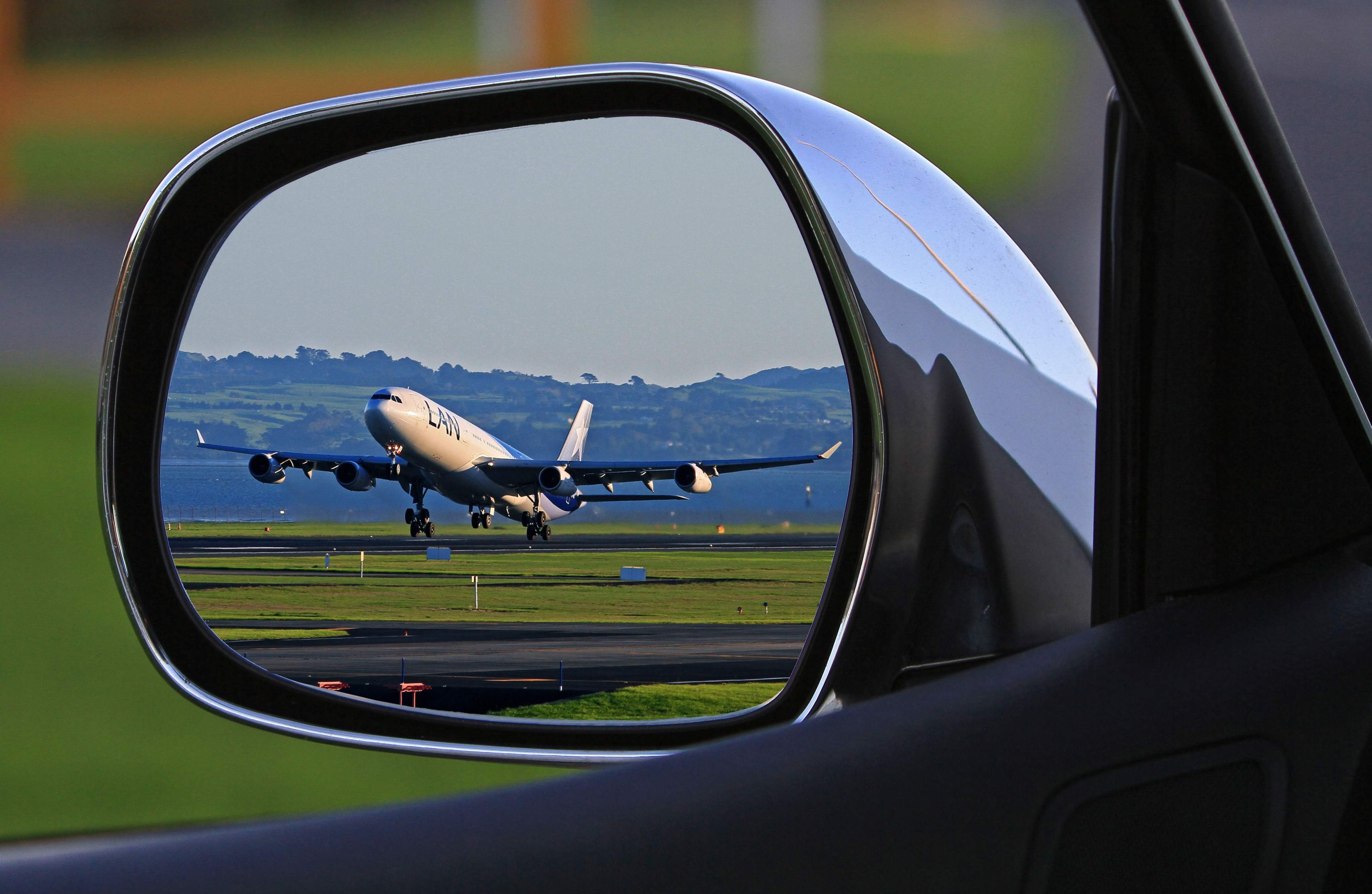 A side mirror shows the reflection of a plane, representing the connection between cars and airport transfers.