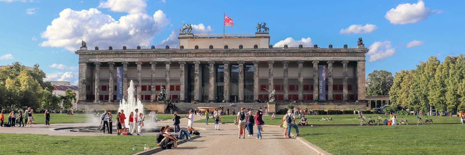 People stroll around the Altes Museum in Berlin, featuring a central fountain and impressive architectural design.