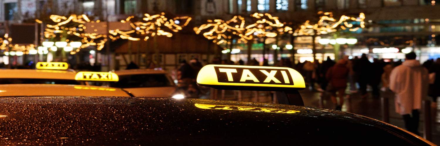 A taxi driving through the illuminated streets of Berlin at night, with city lights reflecting on the vehicle.