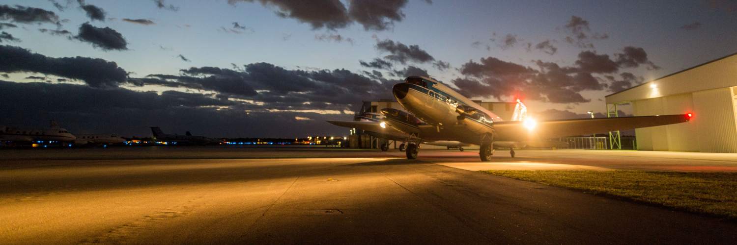 A commercial airplane on the runway at night, with bright lights highlighting its silhouette against the dark background.