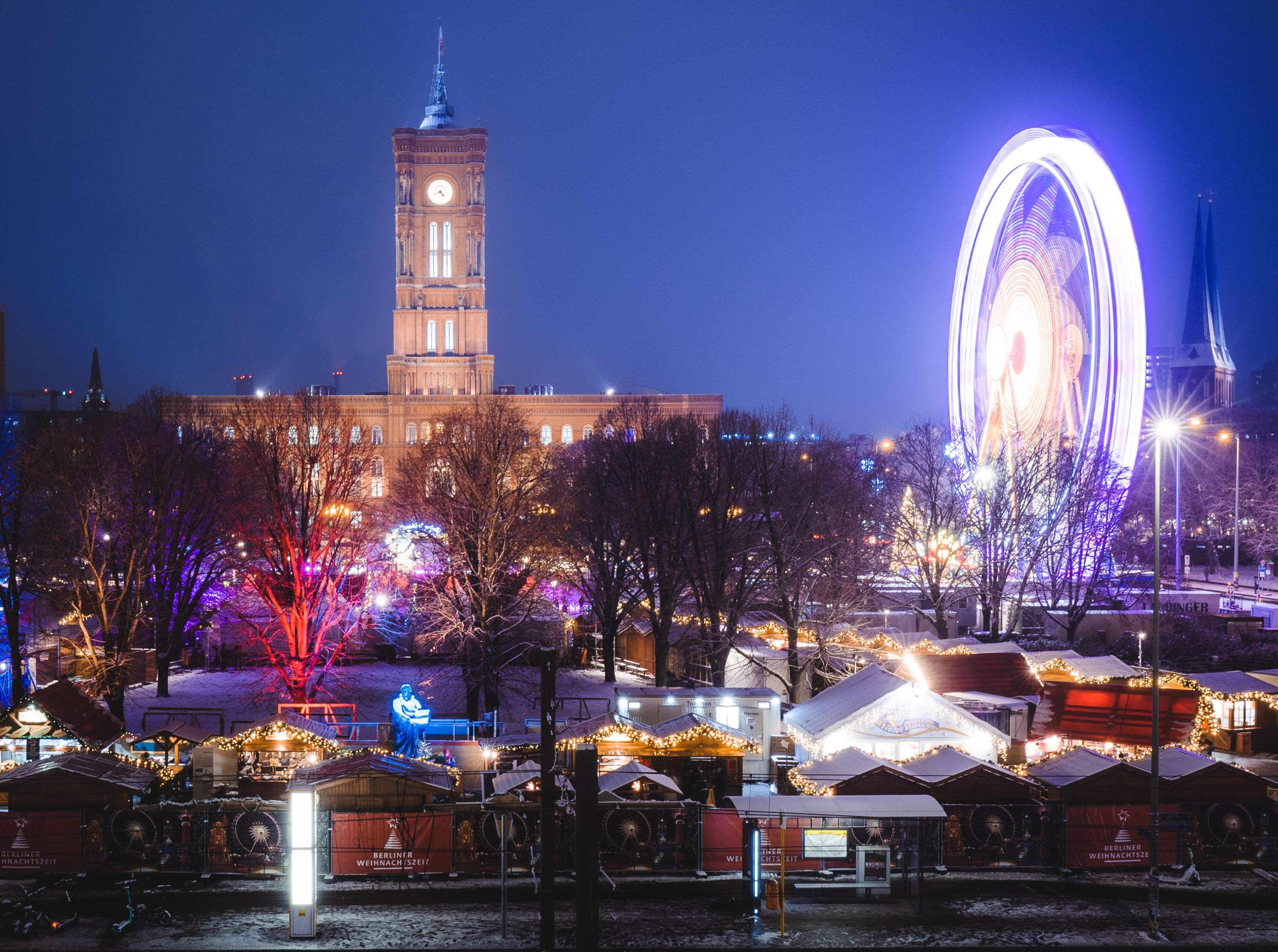 Berlin's Christmas market showcases a grand building with a colorful ferris wheel illuminated in the background.7