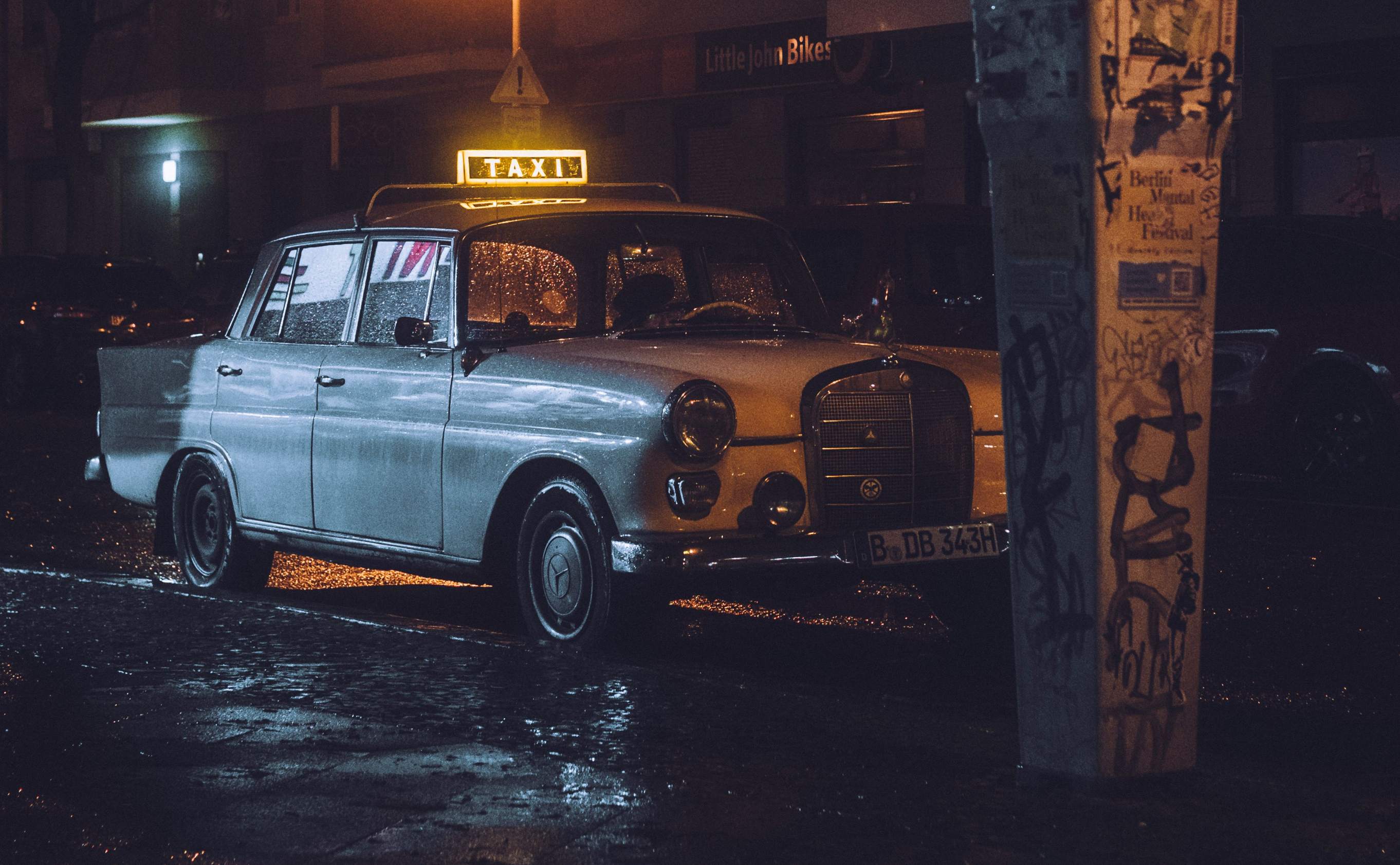 A yellow taxi cab parked on the side of a busy road in Berlin, with city buildings in the background.