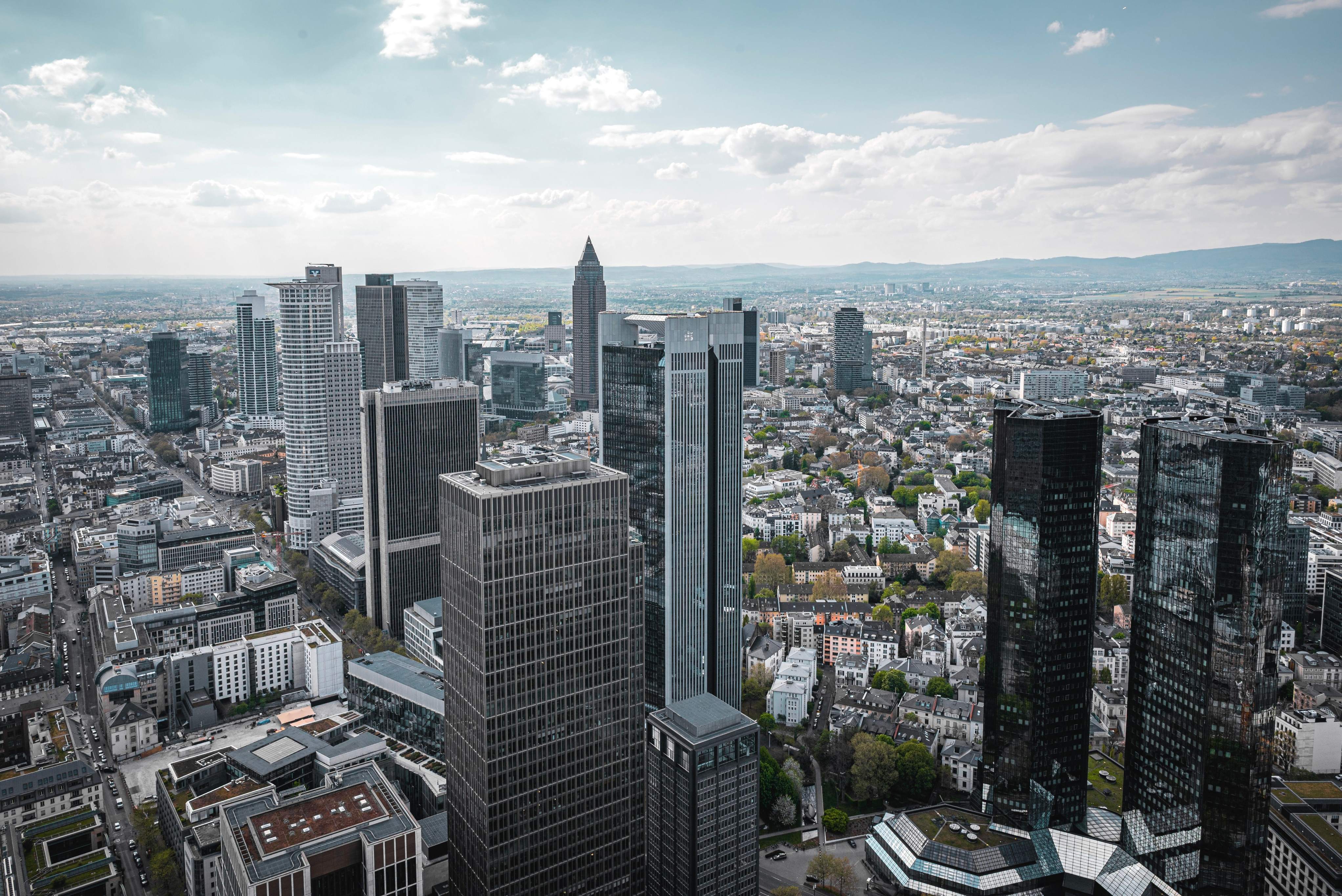 Elevated view of Frankfurt's city skyline, featuring prominent buildings and the Main River flowing through the cityscape.