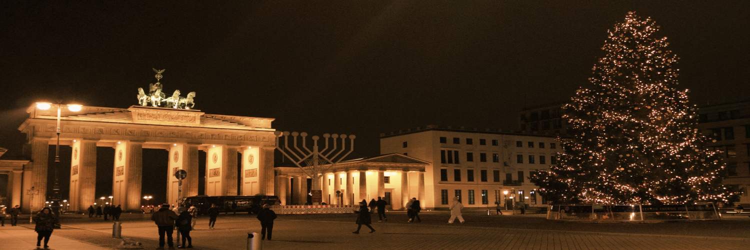 A large Christmas tree stands in front of the Brandenburg Gate, adorned with lights and decorations, set against a winter sky.