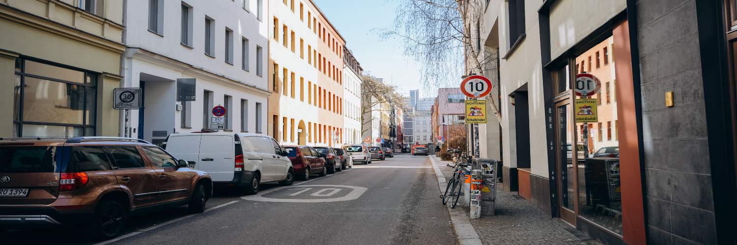 A narrow Berlin street lined with parked cars on both sides, illustrating a typical urban car transfer service area.