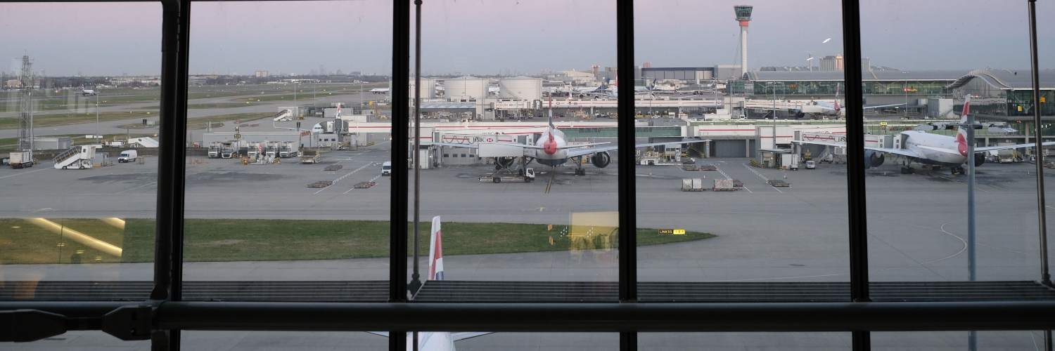 A panoramic view from a window at Heathrow Airport, showcasing runways, aircraft, and terminal buildings.