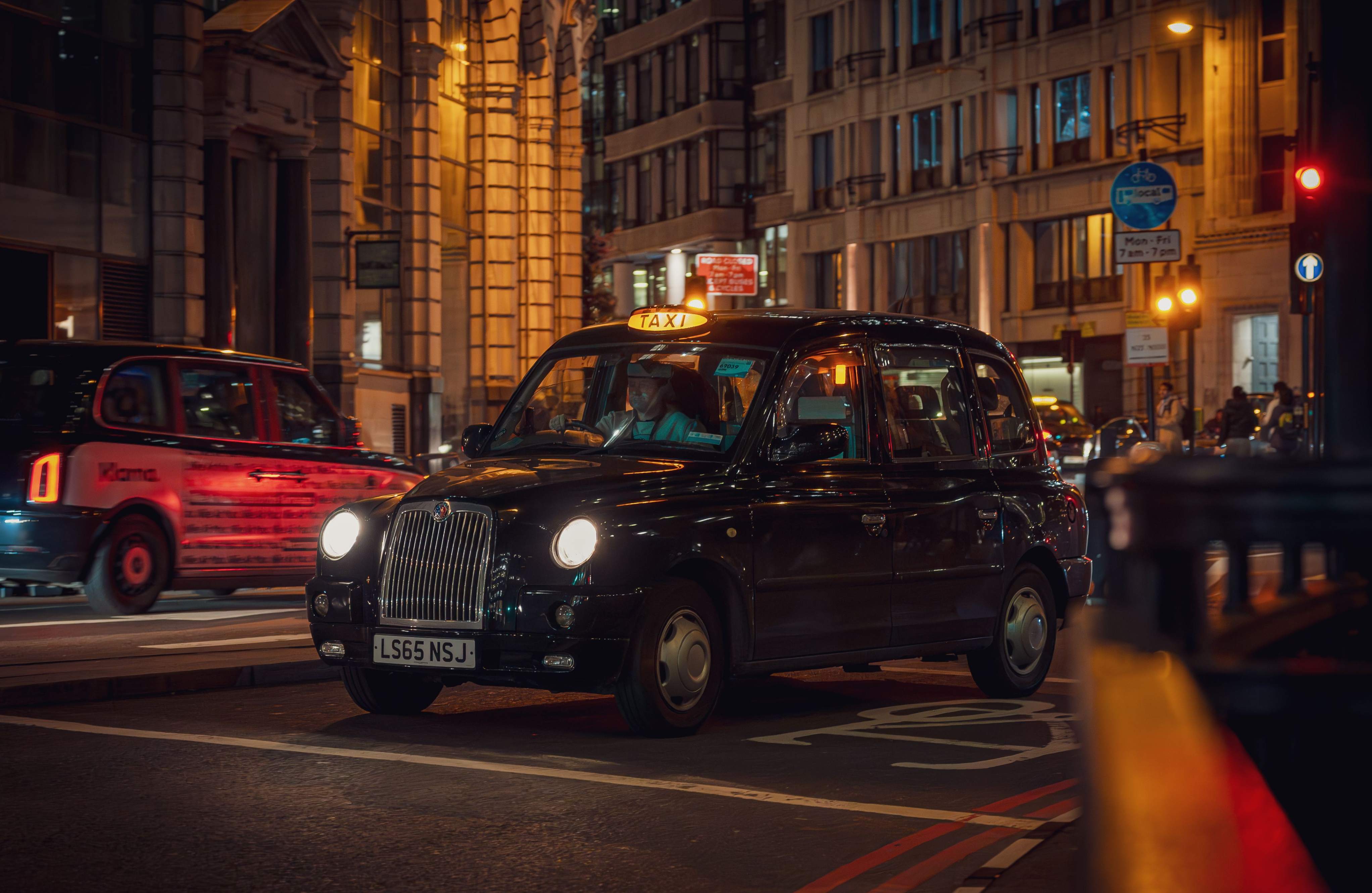 A taxi cab driving down a London street at night, illuminated by streetlights and city lights.