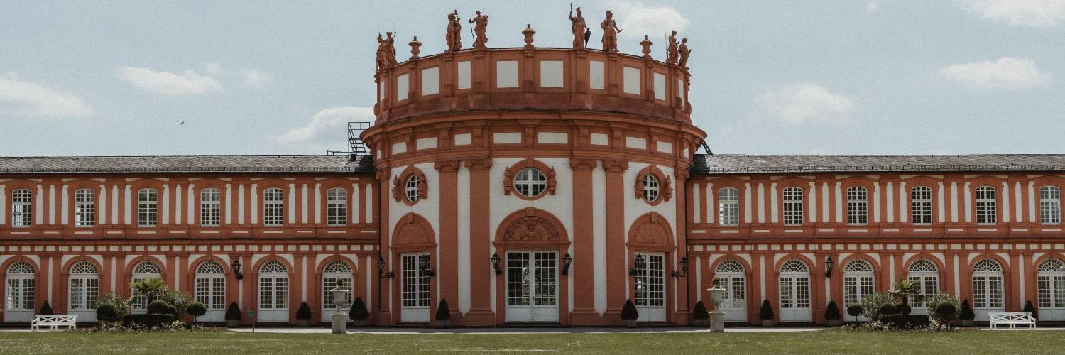 Biebrich Palace in Wiesbaden, featuring a large red facade and a prominent clock tower against a clear blue sky.