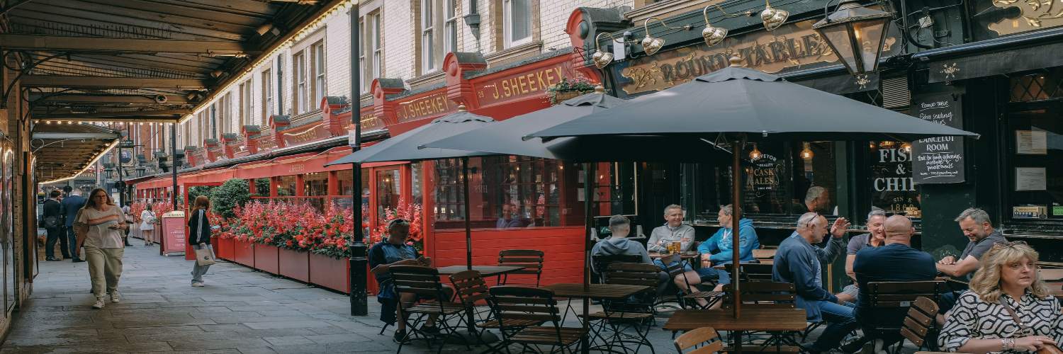 People enjoy outdoor seating at tables with umbrellas in a narrow, charming London street alley.