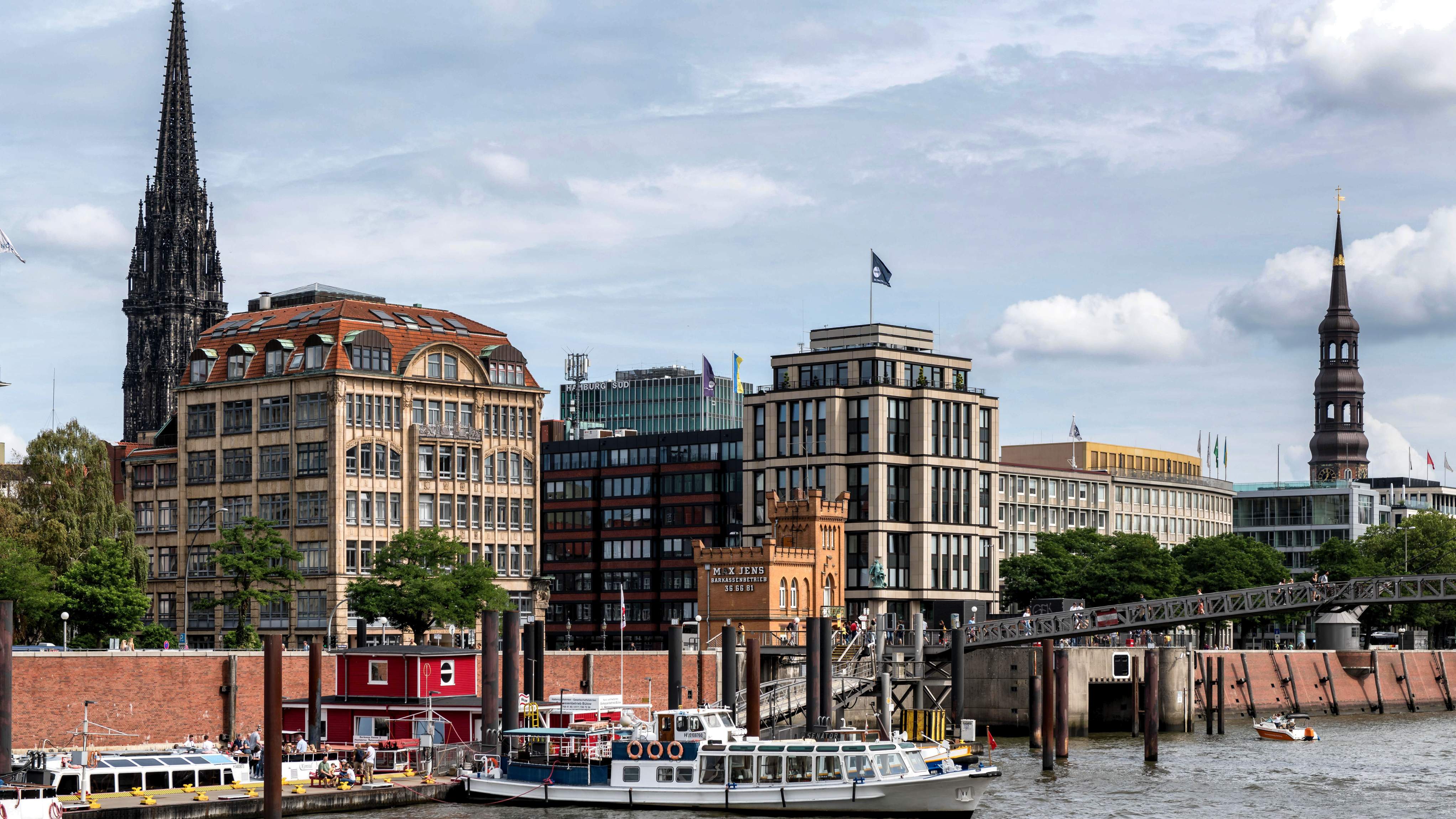 A train crosses a bridge over the Elbe River in Hamburg, with water visible beneath and cityscape in the background.