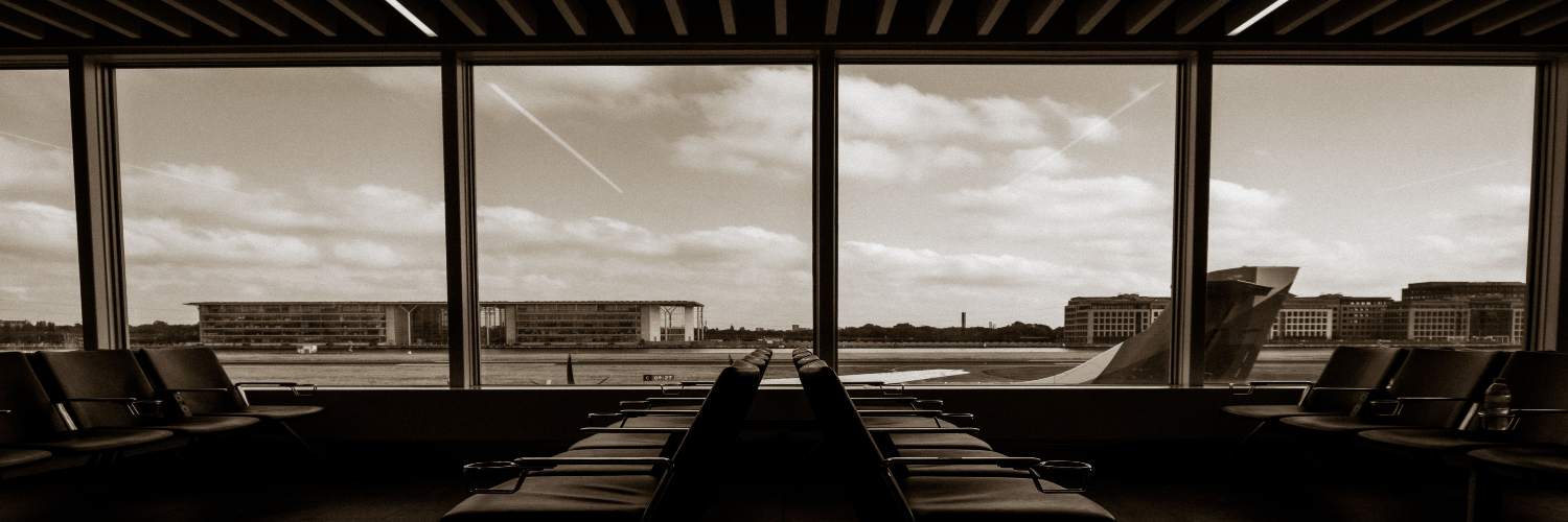 Black and white photo of an airport waiting area featuring rows of empty chairs and minimal decor.