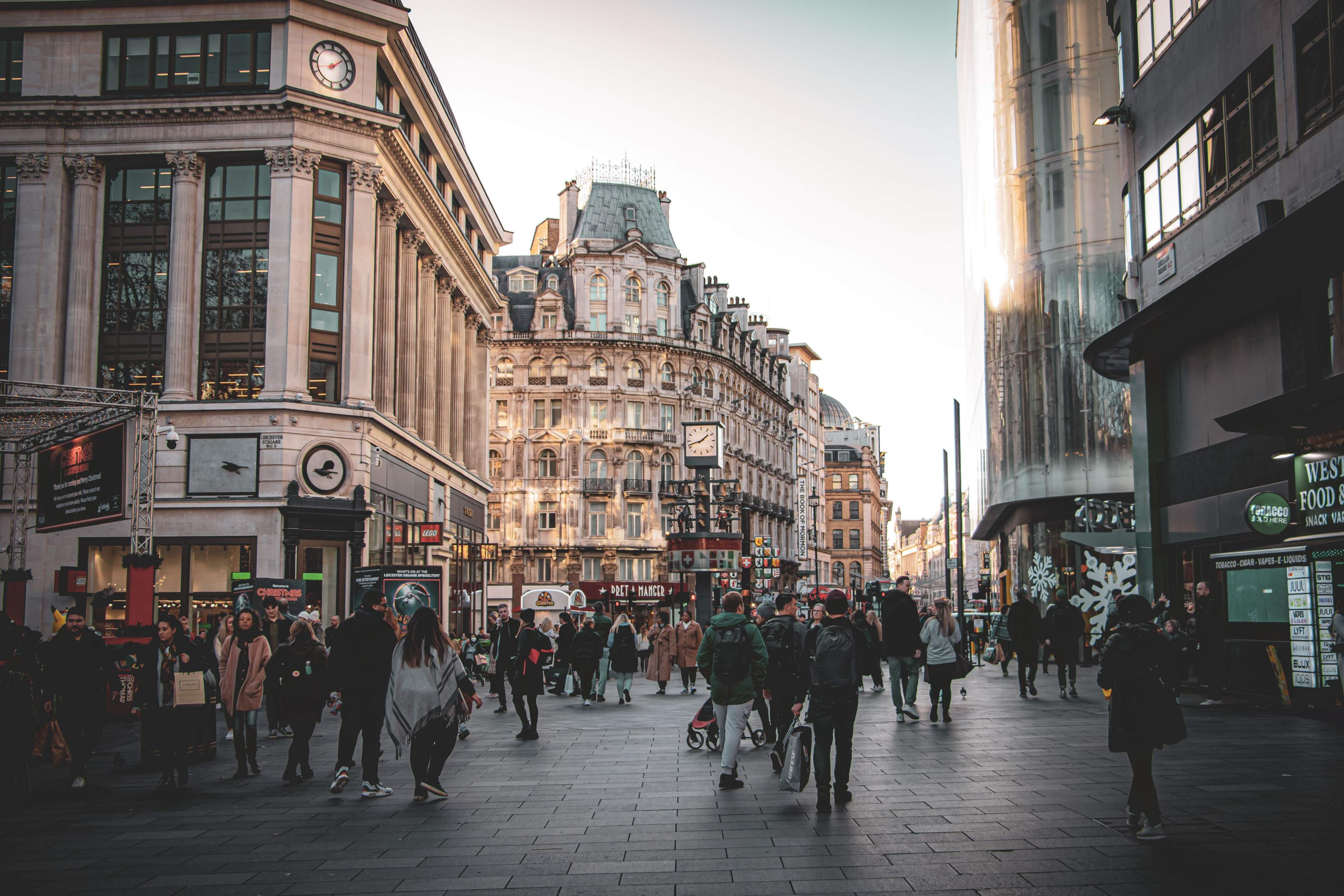 A bustling London street with diverse pedestrians walking amidst shops and historic buildings.