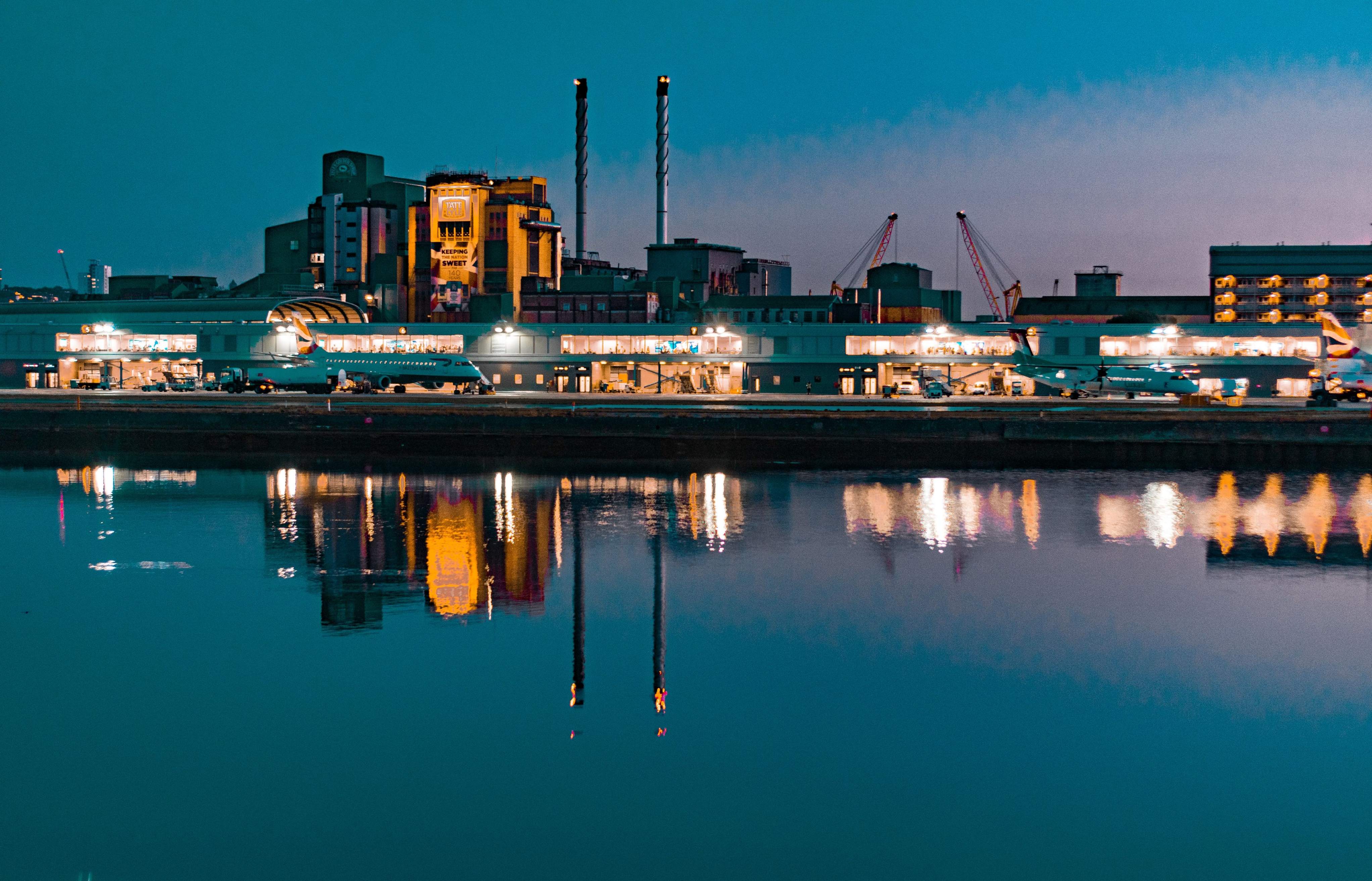The Thames River at dusk, showcasing the city skyline of London near the airport, with lights reflecting on the water.