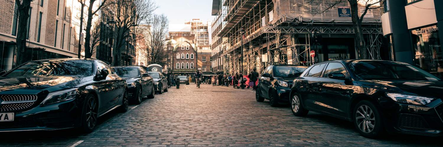 A row of parked cars lined along a cobblestone street in London, showcasing urban architecture and city life.
