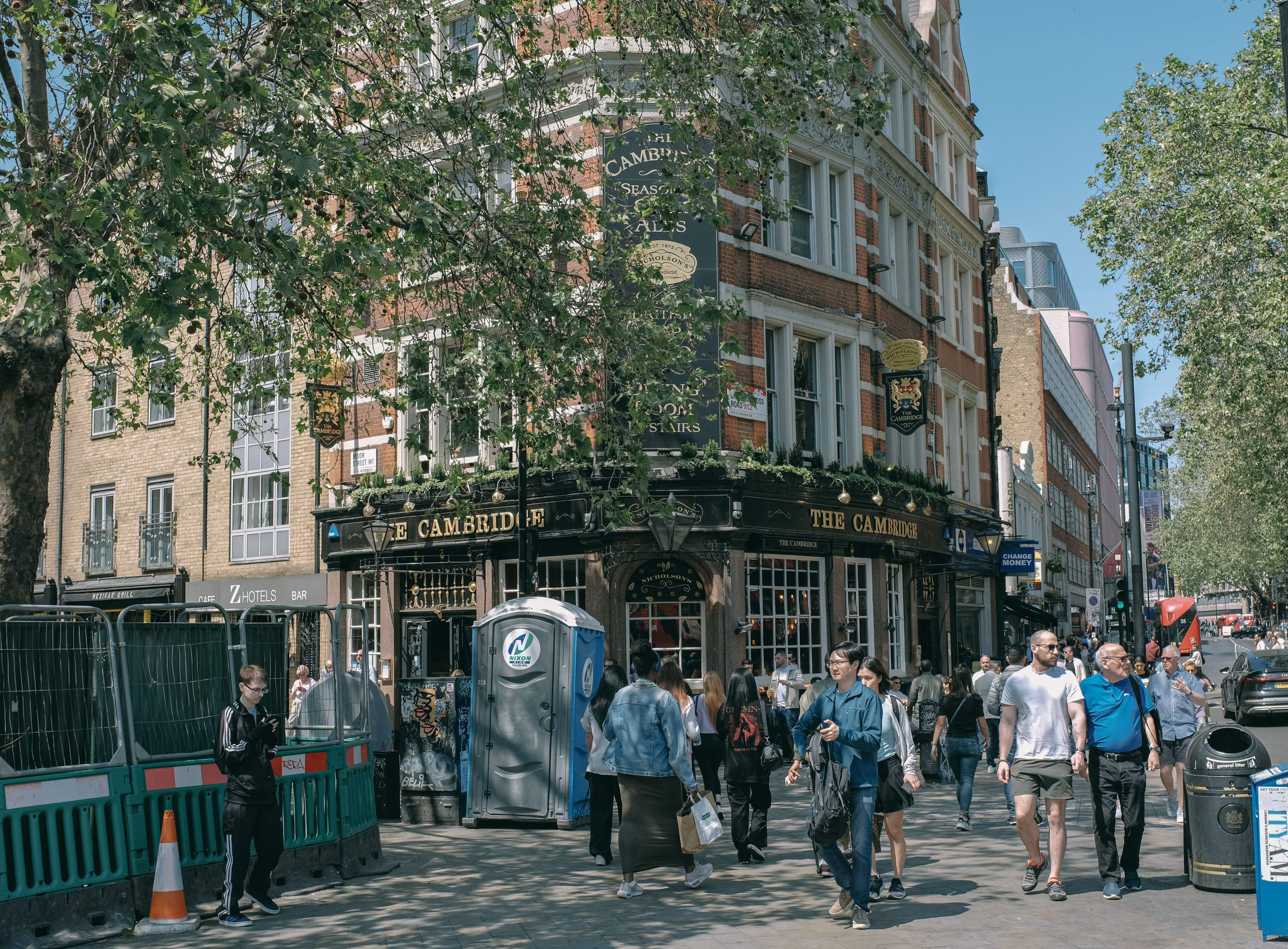 A group of people strolls down a street near a Cambridge pub in London, showcasing a lively urban atmosphere.
