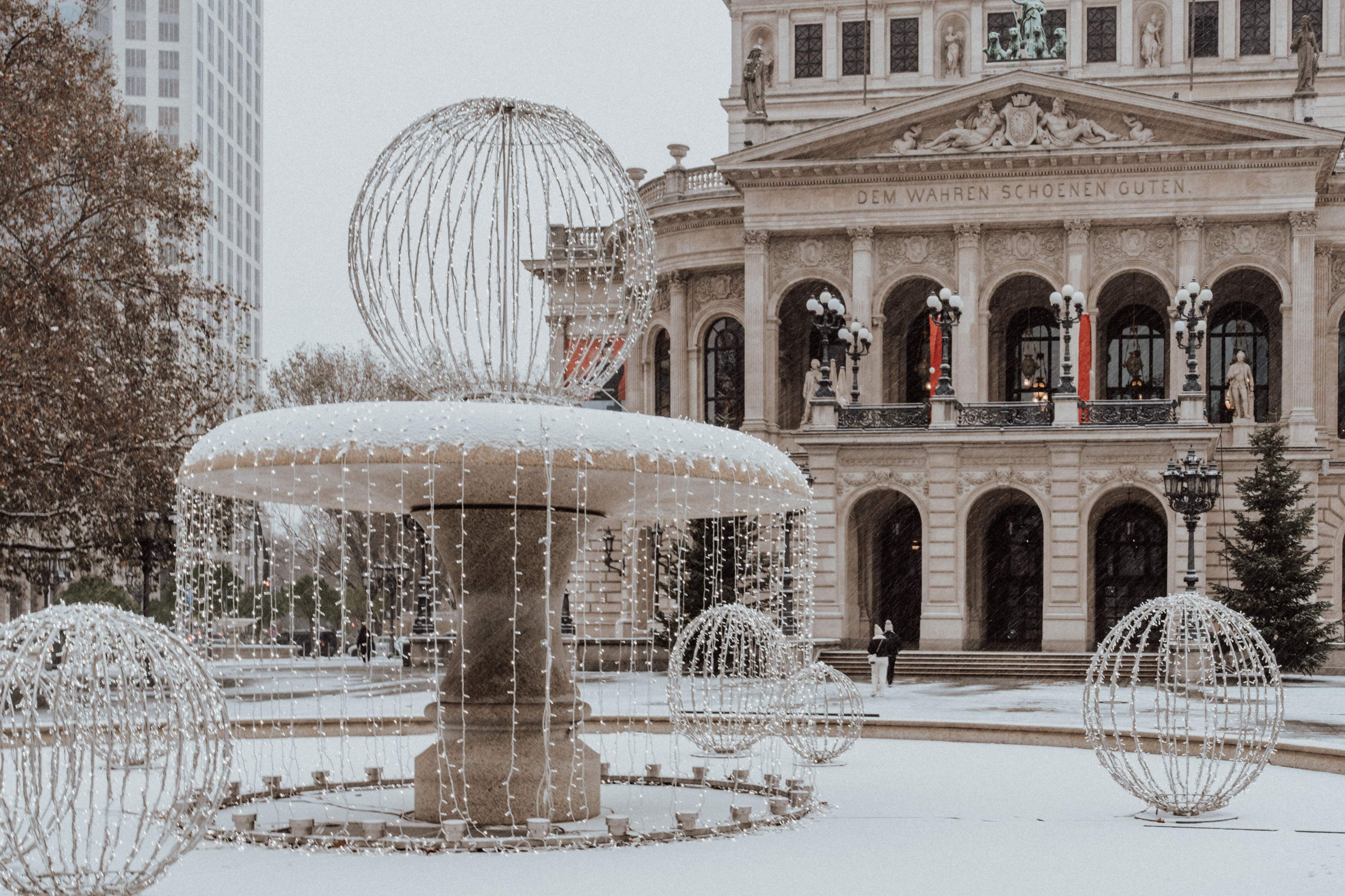 A snow-covered fountain in the foreground with Frankfurt's Alte Oper building visible in the background.