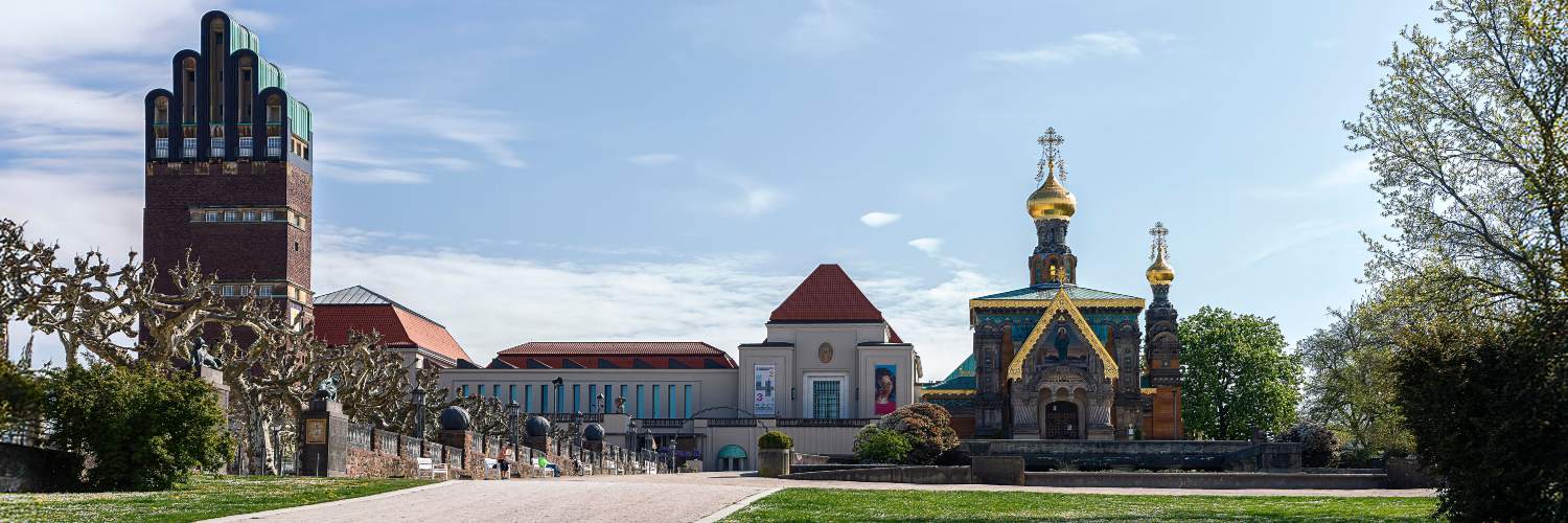 A large historic building with a prominent clock tower, set against a clear sky at Mathildenhöhe in Darmstadt.