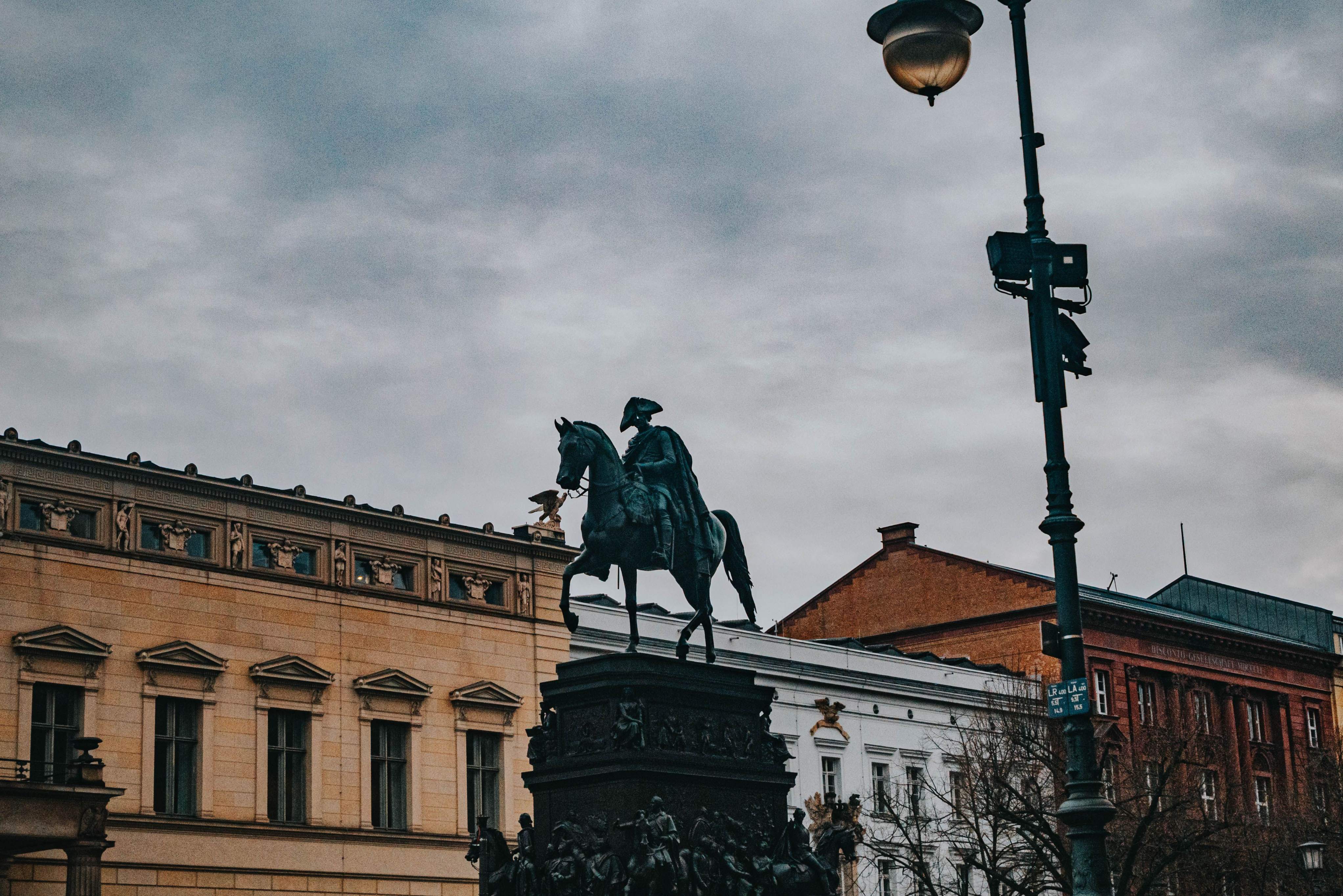 Historic equestrian statue in central Berlin, Germany, surrounded by classical architecture beneath an overcast sky.