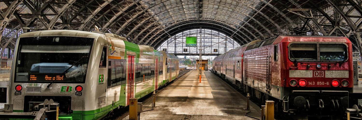 Trains at Leipzig railway station, Germany, with a green-and-white passenger train and a red locomotive on parallel tracks.